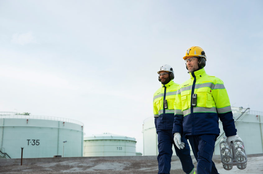 Neste MY refinery employees walking by renewable diesel storage tanks.