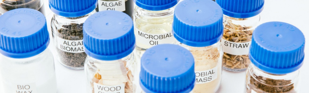 a cluster of clear jars containing renewable raw material samples, including microbial oil, algae biomass, algae oil and straw
